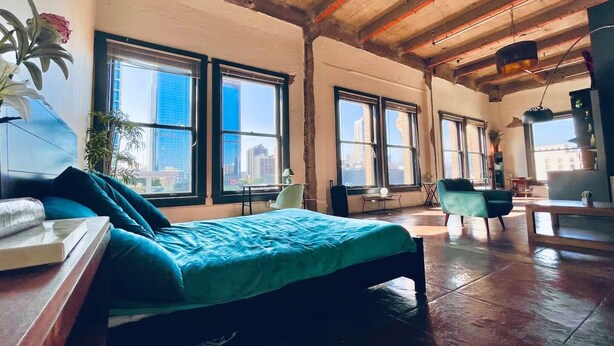 A spacious room with a bed, a desk, and multiple windows offering a view of the cityscape. - Massive Loft Penthouse w best views in Prime DTLA (Los Angeles)