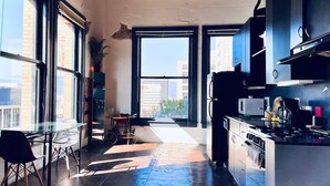 A modern kitchen with large windows, a dining area with a table and chairs, and a view of the cityscape. - Massive Loft Penthouse w best views in Prime DTLA (Los Angeles)