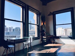 Une pièce dotée de grandes fenêtres, d’une table en verre, d’une chaise, d’une petite table sur laquelle est posée une plante, et d’un miroir.