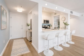 A modern kitchen with white bar stools, a microwave, and a clock on the wall. - Gaslamp District Gem Walk to Dining (San Diego)