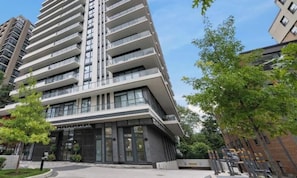 A modern high-rise building with multiple balconies, large windows, and a well-maintained entrance area.