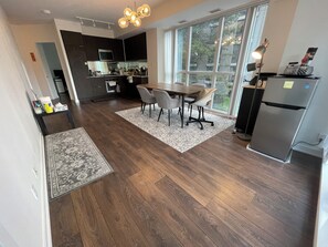 A modern kitchen with dark cabinetry, a dining area with a wooden table and chairs, and a large window providing natural light.