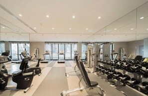 A gym with treadmills, elliptical machines, a weight bench, and free weights.