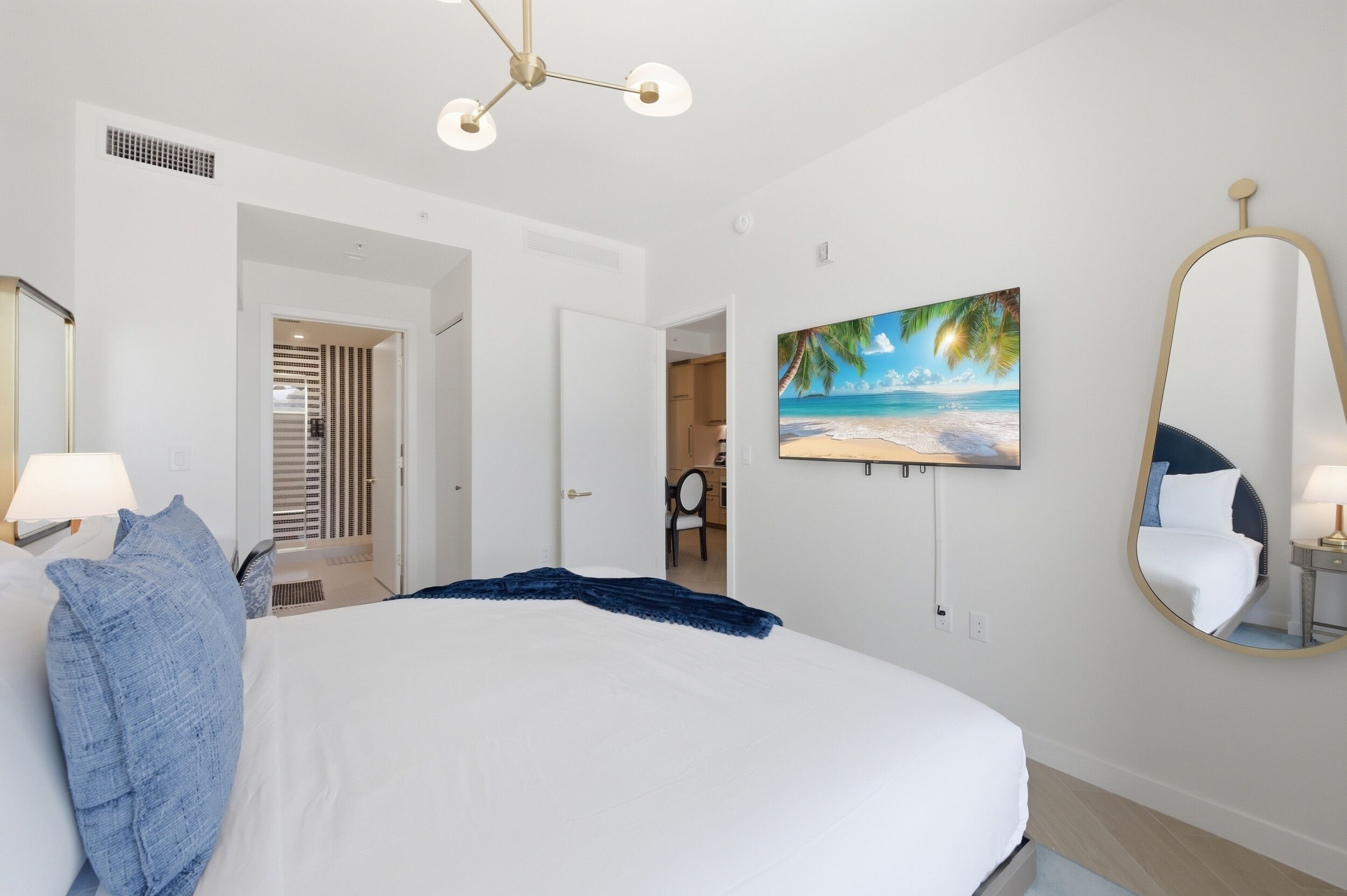 A bedroom with a bed, a painting, a mirror, and a door leading to another room.
