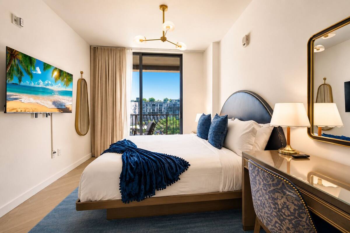 A hotel room with a bed, a desk, a chair, a large window, and a painting.