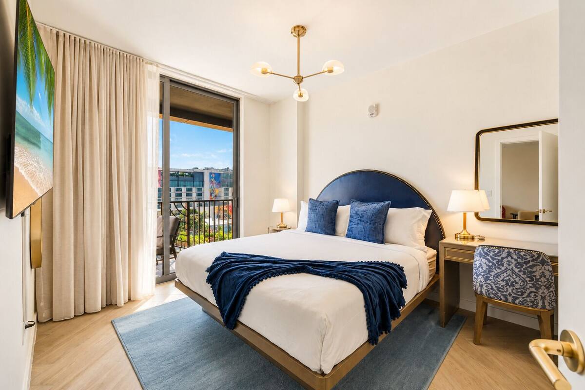 A hotel room with a large bed, a balcony with a view, a desk with a lamp, and a chair.