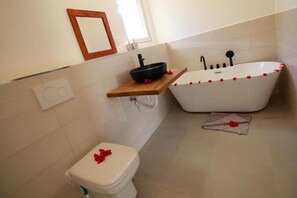 A bathroom with a white bathtub, a toilet, and a wooden shelf with a black basin. - Shiri Beach Resort Fumba Zanzibar (Fumba)