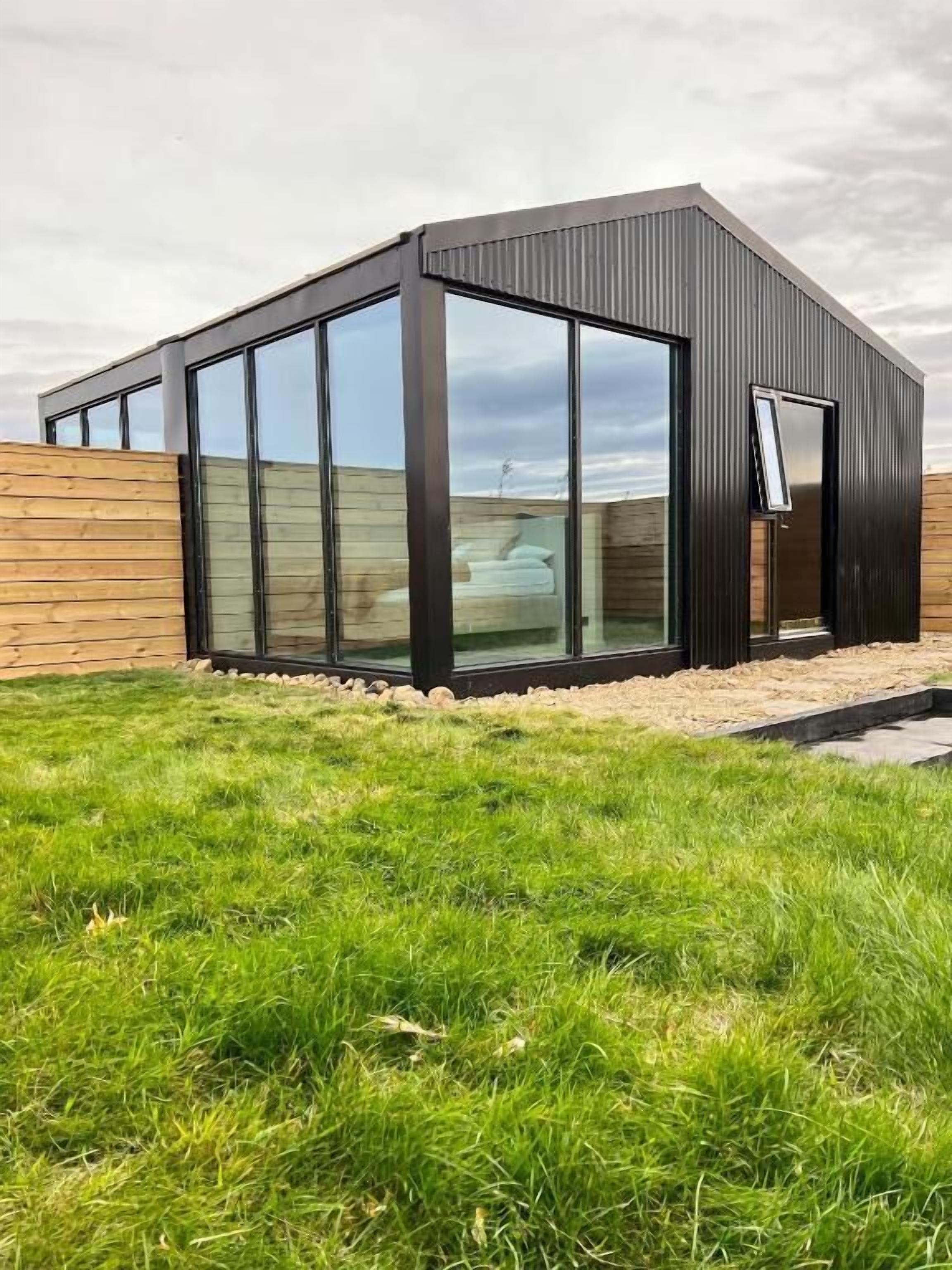 A modern building with large glass windows, a sloped roof, and a wooden fence.