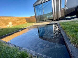 A modern building with large windows, a small water feature, and a wooden fence. - Night & Day Lodge (Borgarbyggð)