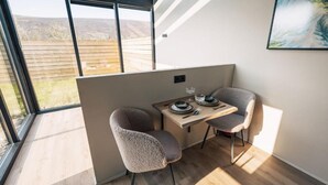 Ein modernes Zimmer mit großem Fenster, einem Holztisch, zwei Stühlen und einem Gemälde an der Wand.