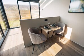 A modern room with a large window, a wooden table, two chairs, and a painting on the wall. - Night & Day Lodge (Borgarbyggð)