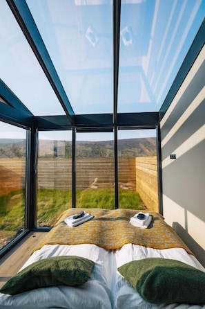 Une chambre avec une grande fenêtre, un lit avec des oreillers verts et une vue sur un paysage.