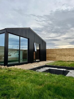 A modern building with large glass windows, a wooden exterior, and a grassy area with a stone pathway. - Night & Day Lodge (Borgarbyggð)