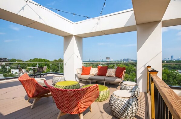 A rooftop terrace with a sofa, chairs, and round tables, offering a city view.