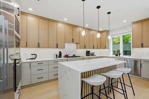 Eine moderne Küche mit Holzschränken, einer weißen Kücheninsel mit Barhocker und Pendelleuchten.