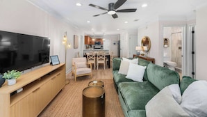 A modern living room with a flat-screen TV, a green sofa, a wooden entertainment unit, and a ceiling fan. - The Pinewood · Dog-Friendly 30A Home for 8 (Santa Rosa Beach)