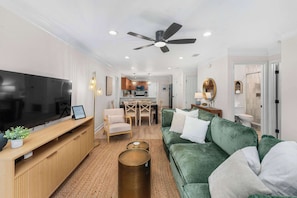 A modern living room with a flat-screen TV, a green sofa, a wooden entertainment unit, and a ceiling fan. - Dog-Friendly 30A Home | Sleeps 8 | Fire Pit Yard (Santa Rosa Beach)