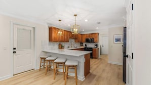 A kitchen with wooden cabinets, a white island with stools, and pendant lighting. - The Pinewood · Dog-Friendly 30A Home for 8 (Santa Rosa Beach)