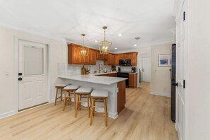 A kitchen with wooden cabinets, a white island with stools, and pendant lighting. - Dog-Friendly 30A Home | Sleeps 8 | Fire Pit Yard (Santa Rosa Beach)
