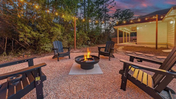 An outdoor seating area with Adirondack chairs, a fire pit, and string lights. - The Pinewood · Dog-Friendly 30A Home for 8 (Santa Rosa Beach)