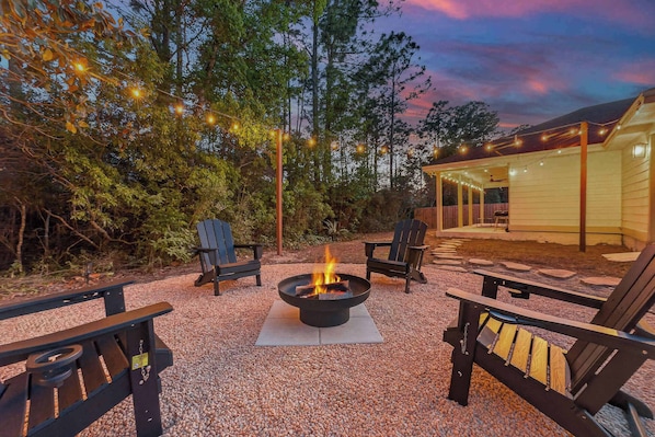 An outdoor seating area with Adirondack chairs, a fire pit, and string lights. - Dog-Friendly 30A Home | Sleeps 8 | Fire Pit Yard (Santa Rosa Beach)