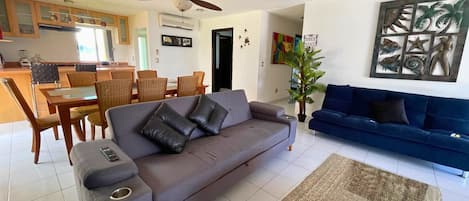 Una sala de estar con sofá, una mesa de centro, un comedor con sillas y una mesa, y una cocina al fondo.