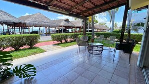 A covered outdoor area with thatched umbrellas, chairs, and a view of the sea.