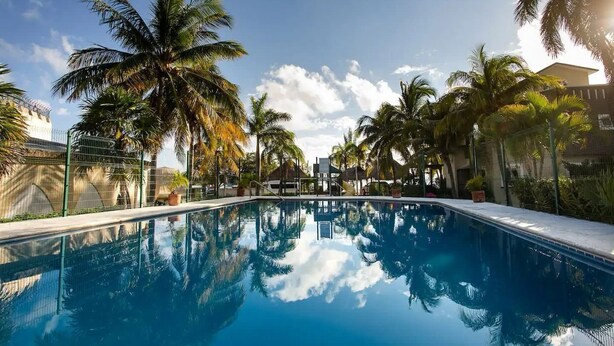 A clear swimming pool surrounded by palm trees and a clear sky.