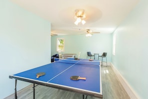 Une pièce avec une table de ping-pong, deux chaises, un ventilateur de plafond et une fenêtre donnant sur un beau paysage.