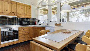 Eine moderne Küche mit Holzschränken, einem eingebauten Backofen und einem Essbereich mit großem Tisch und Stühlen.