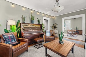 Ein Wohnzimmer mit Klavier, Ledersessel, Hocker und Couchtisch aus Holz.