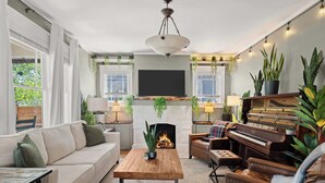 Una sala de estar con sofá, mesa de centro, chimenea, piano y varias plantas.