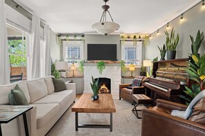 Ein Wohnzimmer mit Sofa, Couchtisch, Kamin, Klavier und diversen Pflanzen.