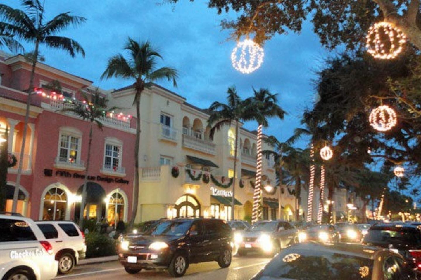 A street lined with palm trees and buildings with illuminated signs, suggesting a lively urban area.
