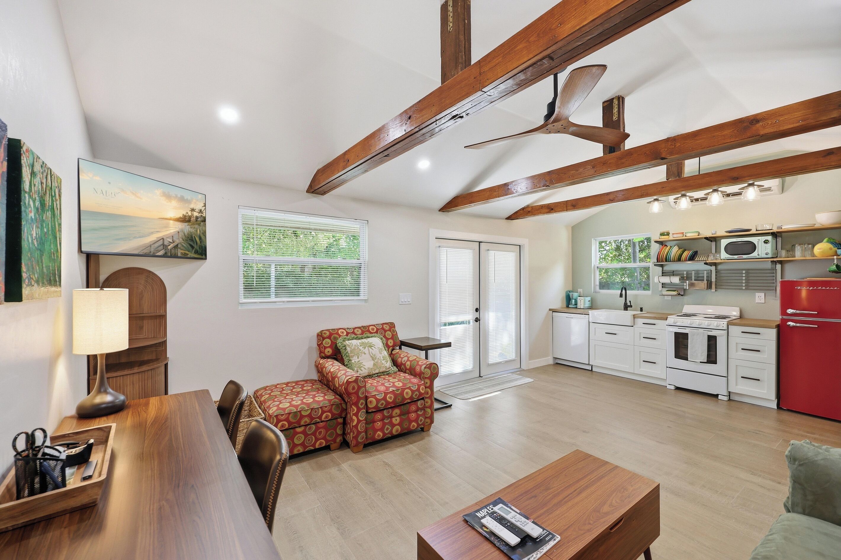 A spacious living area with a wooden ceiling, a dining table, a sofa, and a kitchen with white appliances.