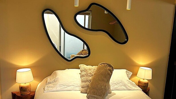 A bed with a white comforter, two bedside lamps, and a wall-mounted mirror. - Private Escazú Studio Chill Pad (Escazu)