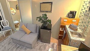 A compact living space with a grey sofa, a small fridge, a laptop on a wooden table, and a sink area. - Private Escazú Studio Chill Pad (Escazu)
