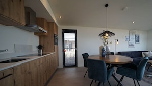 A modern kitchen with wooden cabinets, a dining area with a round table and chairs, and a living area with a sofa.