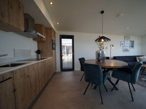 Een moderne keuken met houten kastjes, een eethoek met een ronde tafel en stoelen, en een zithoek met een bank.