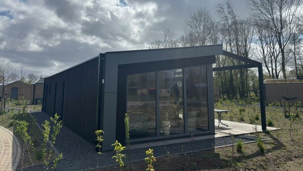 A modern building with large glass windows, a flat roof, and a paved outdoor area with young plants.