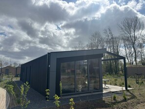 Een modern gebouw met grote glasramen, een plat dak en een verhard buitengebied met jonge planten.