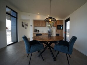 A modern kitchen with wooden cabinets, a round dining table with blue chairs, and a pendant light. - Holiday Home in Enkhuizen With Terrace (Enkhuizen)