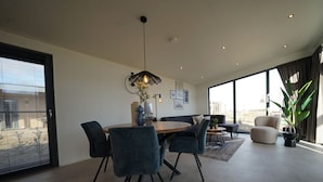 A spacious living area with a dining table, chairs, a sofa, and a large window offering a view.