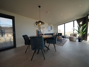 A spacious living area with a dining table, chairs, a sofa, and a large window offering a view. - Holiday Home in Enkhuizen With Terrace (Enkhuizen)