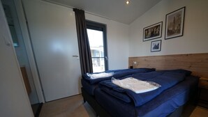 A bedroom with a bed, a wooden headboard, a window with curtains, and a door.