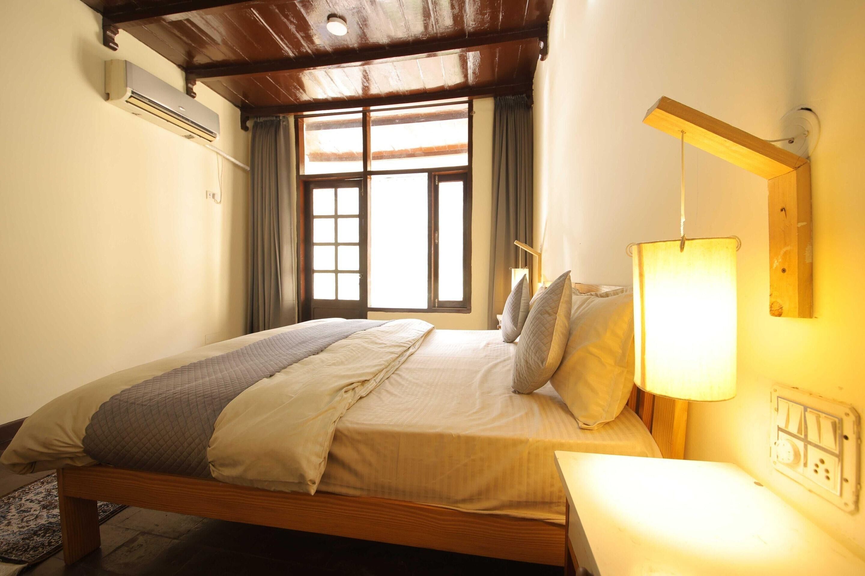 A single bed with a wooden frame, a bedside table, a lamp, and a window with curtains.