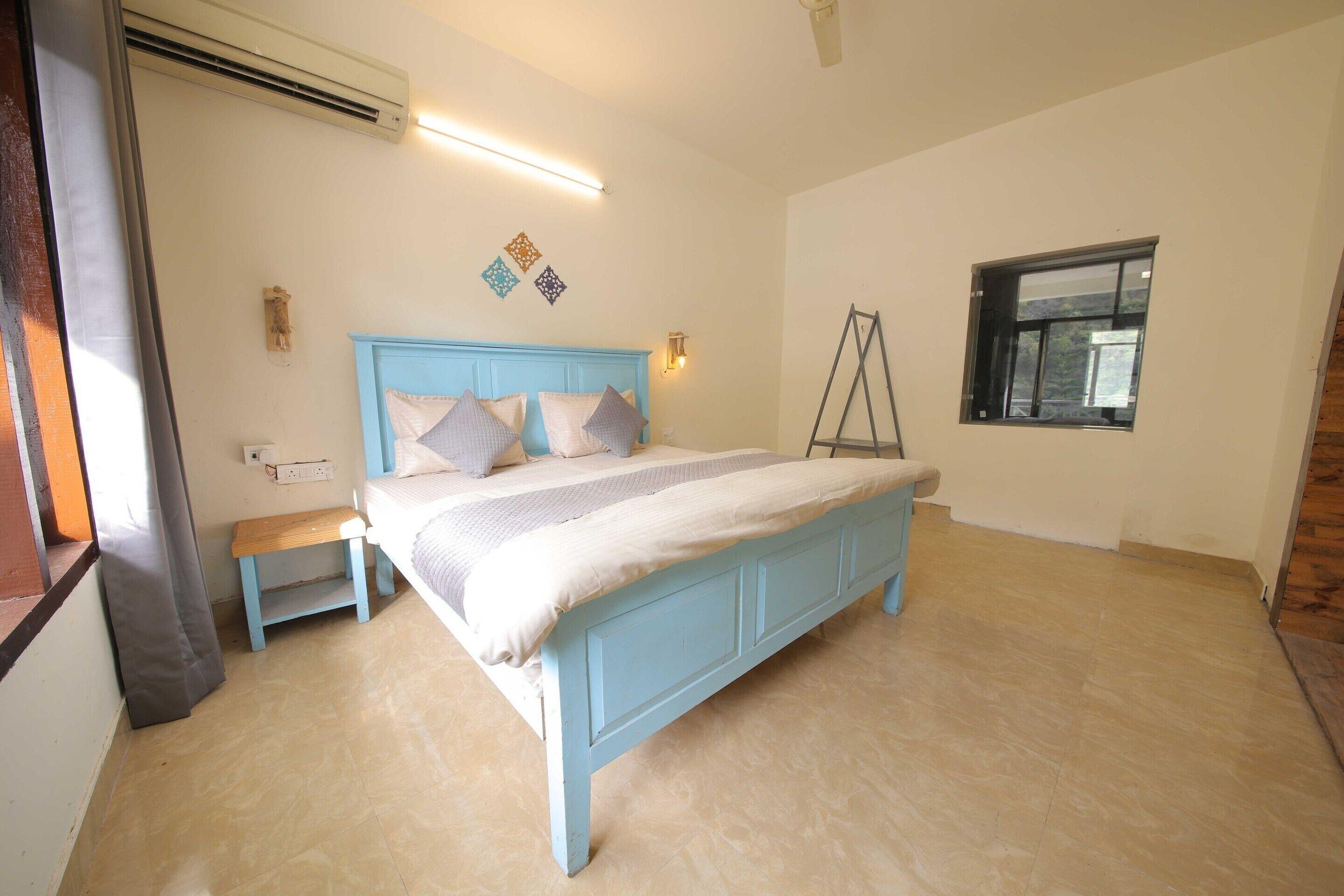 Quarto com cama, mesa de cabeceira, luminária na parede, aparelho de ar condicionado, janela e peças decorativas na parede.
