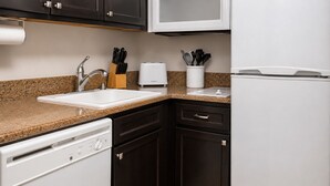 Uma cozinha com lava-louças branca, armários escuros, bancada de granito, micro-ondas branco e torradeira.