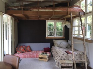 Une pièce rustique avec un lit en mezzanine, un petit canapé, une échelle en bois et une fenêtre donnant sur les arbres.