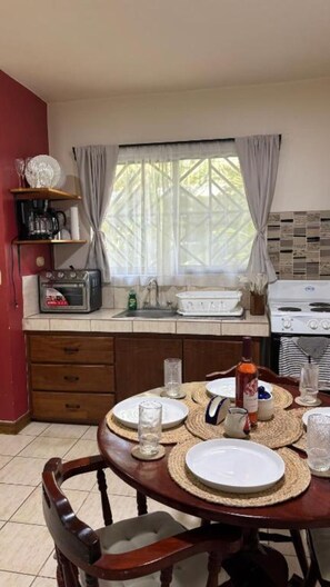 Une cuisine avec une table à manger pour deux personnes, un fourneau et une fenêtre avec des rideaux.